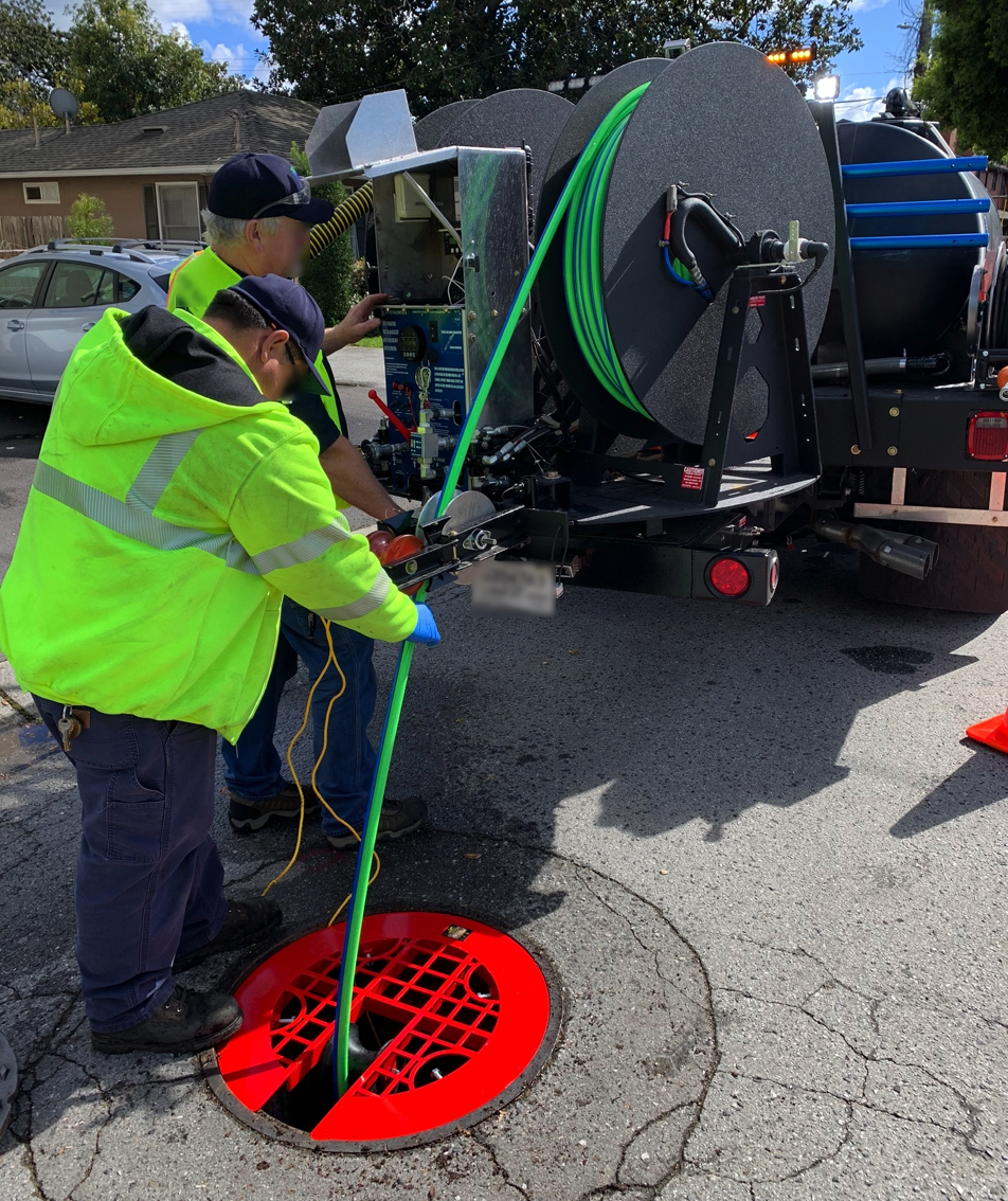 Photo of worker in high-visibility jacket feeding hose into manhole on street