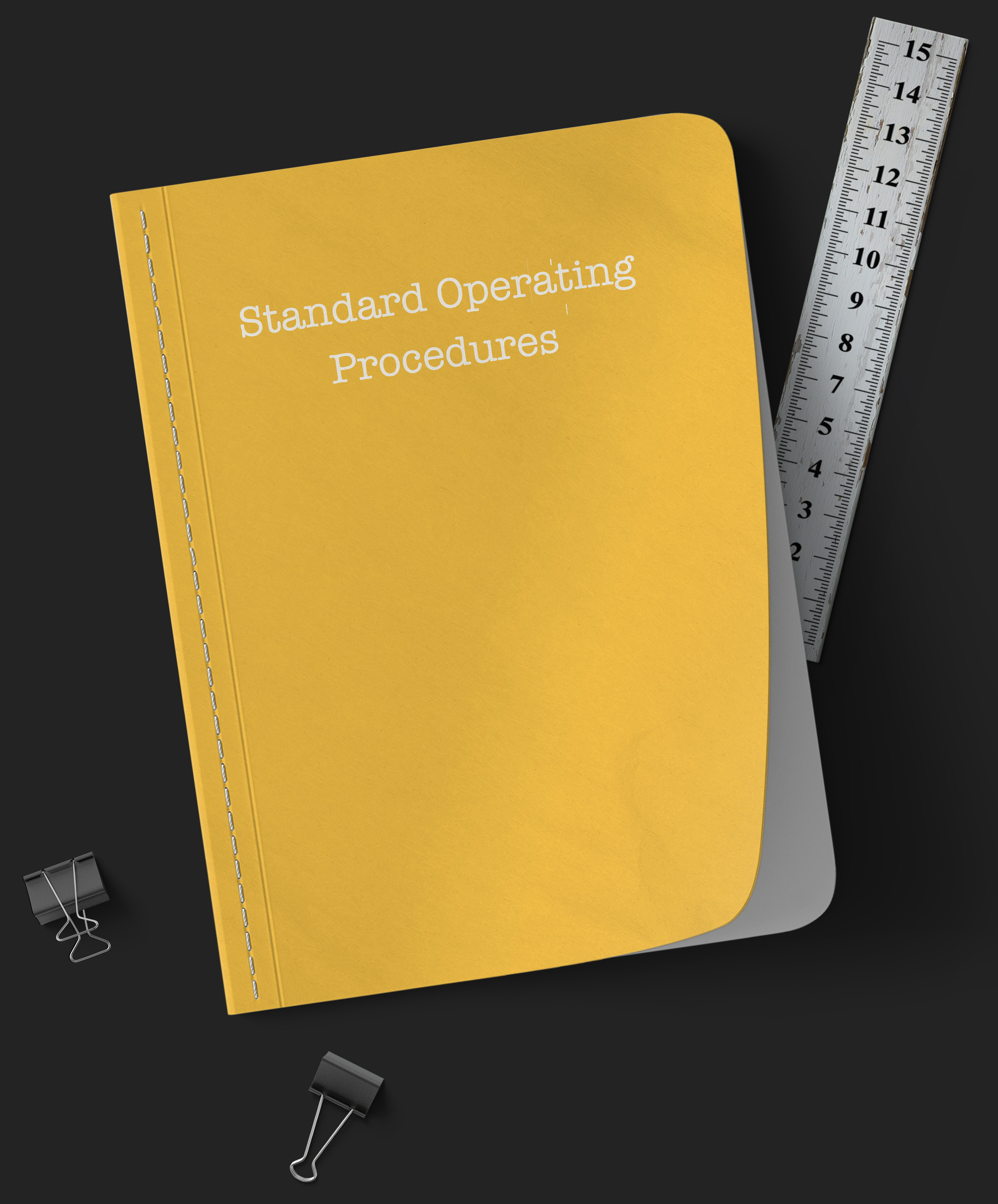 Yellow notebook with Standard Operating Procedures typed on the cover, with a metal ruler and black binder clip.